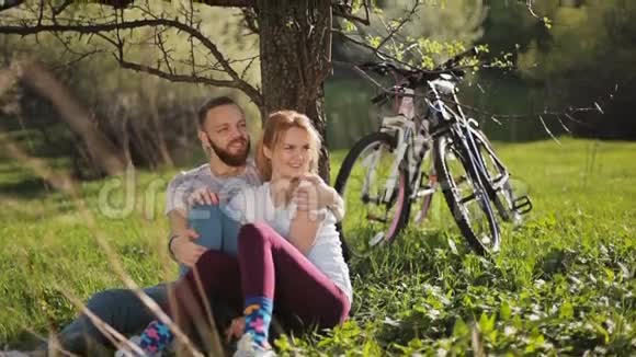骑自行车的男人和女人坐在他自行车的背景下的一棵树下视频的预览图