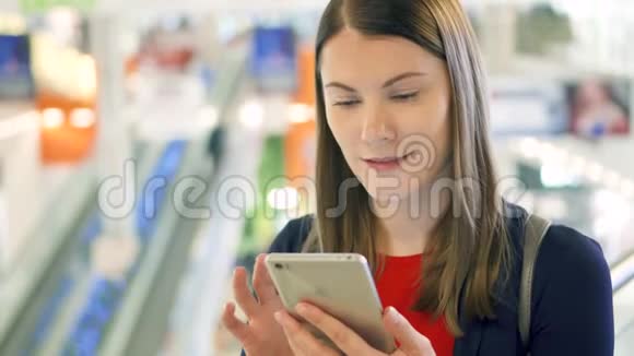 年轻漂亮的女人站在购物中心微笑用她的智能手机和朋友聊天视频的预览图