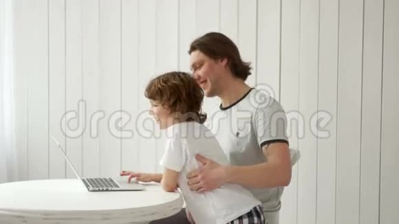 一个忙碌的年轻人在家里用笔记本电脑工作也照顾他的儿子视频的预览图