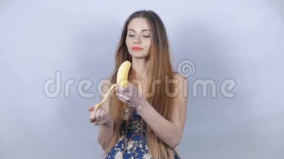年轻开朗的女人在工作室里用红色口红剥皮和吃香蕉视频的预览图
