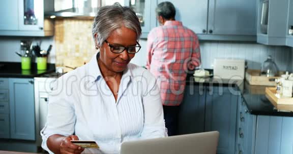 一位在家厨房用笔记本电脑上网购物的老妇人视频的预览图