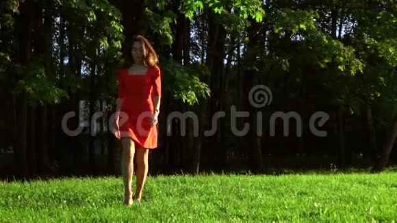 瘦削的黑发女孩穿着红色连衣裙在公园的草地上散步慢动作视频120fps视频的预览图
