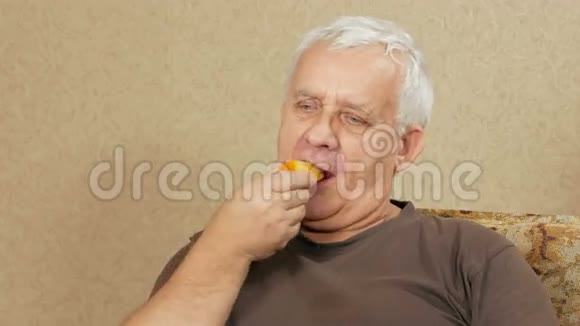 超重老人在家里的沙发上吃水果他切下一块柿子咬了几口健康食品视频的预览图