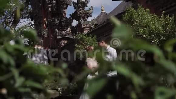 巴厘岛佛寺附近的新婚夫妇牵手拥抱浪漫的婚礼视频的预览图