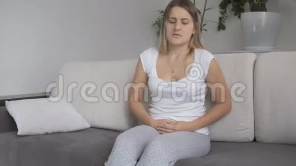 月经痛的年轻女子坐在沙发上双手抱着肚子视频的预览图