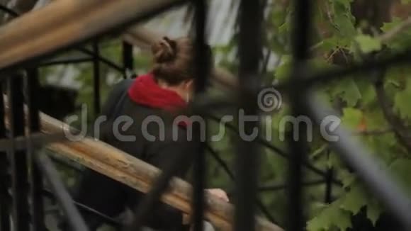 穿着夹克和红领巾的女人在大自然的背景下走下金属楼梯视频的预览图