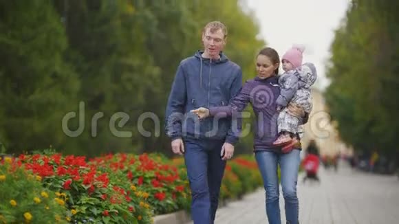 幸福的家庭秋天公园里的爸爸妈妈和小女孩带着鲜花在小巷里散步视频的预览图