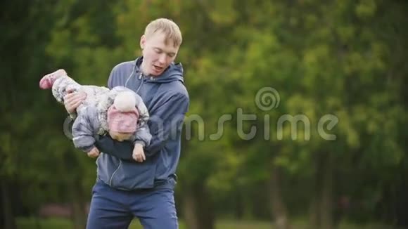 快乐的家庭爸爸妈妈和小女孩在秋天的公园散步妈妈拥抱爸爸和宝宝慢动作视频的预览图