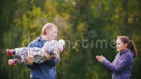 幸福的家庭爸爸妈妈和小女孩在秋天公园散步玩和拍手慢动作视频的预览图