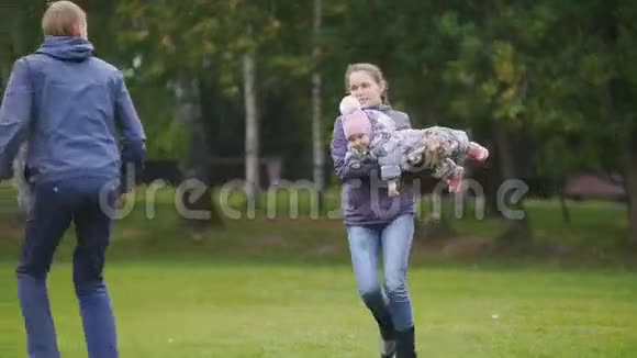 幸福的家庭爸爸妈妈和小女孩在秋天的公园散步在草地上跑步和玩耍视频的预览图