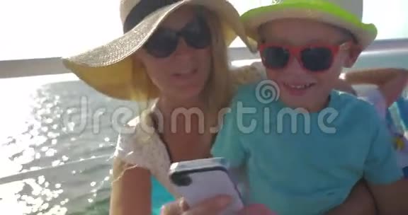 年轻的女人和儿子坐着摩托艇在智能手机里看东西视频的预览图