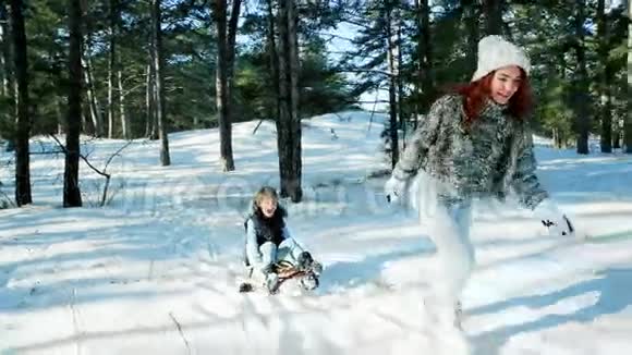 在森林里雪橇妈妈在冬天把儿子卷在雪橇上幸福的家庭为母亲和母亲提供有趣的娱乐视频的预览图