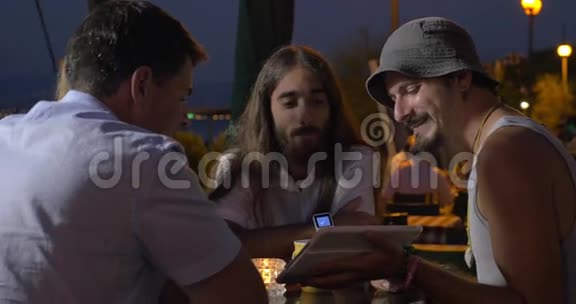 一群朋友晚上坐在桌子旁看着平板电脑上的视频其中一个人在聊天视频的预览图