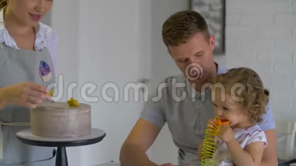 幸福的家庭坐在厨房里妈妈在装饰水果蛋糕视频的预览图