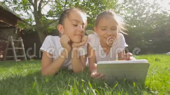 两个微笑的女孩躺在草地上用数码平板电脑的肖像视频的预览图
