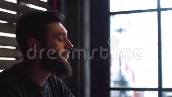 年轻人在咖啡馆的窗户旁边喝咖啡有胡子的人视频的预览图