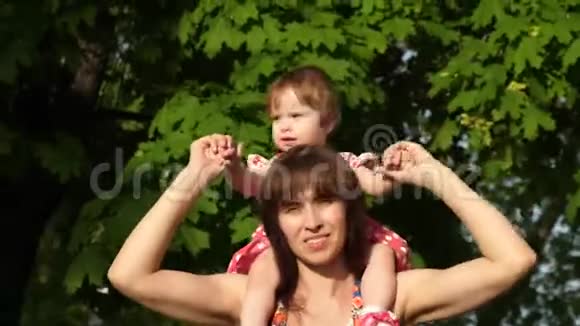 妈妈背着小女儿带着孩子在公园散步视频的预览图