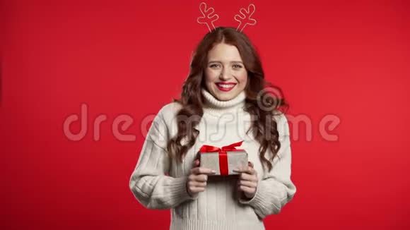 年轻可爱的女孩微笑着拿着礼物盒在红色的工作室背景视频的预览图