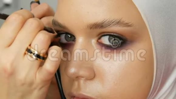 女化妆师造型师用年轻模特的特殊化妆画笔使化妆时尚粉红烟熏的眼睛视频的预览图