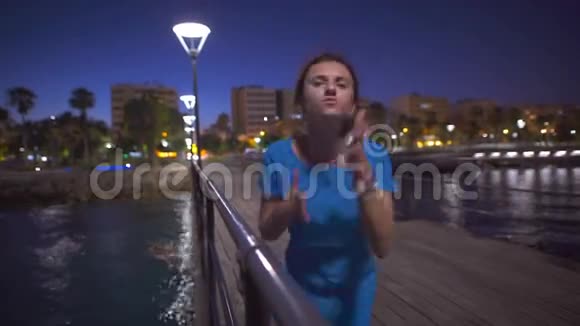 一位美丽的女人在海边跳舞看着夜晚的城市全景视频的预览图