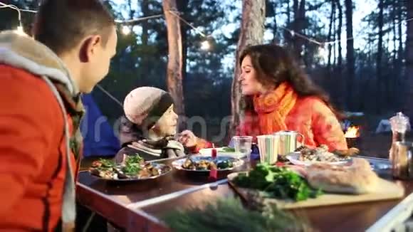 幸福的年轻一家人坐在餐桌旁交谈秋天的森林视频的预览图