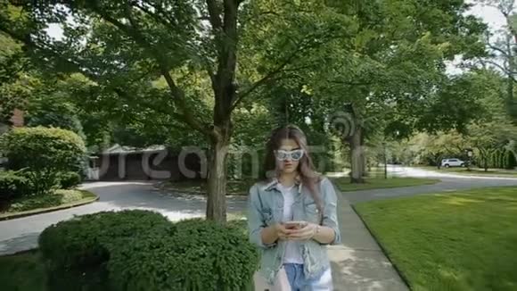 戴着绿色眼镜的女士在公园里散步用手机聊天视频的预览图