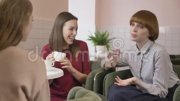 三个年轻女孩坐在咖啡馆里笑着微笑着朋友陪伴闲聊对话讨论女朋友视频的预览图