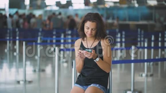 乘客机场里的女人用智能手机等着她的航班微笑着视频的预览图