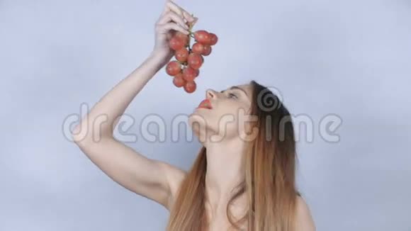 漂亮的年轻女人在工作室里吃一串红葡萄视频的预览图