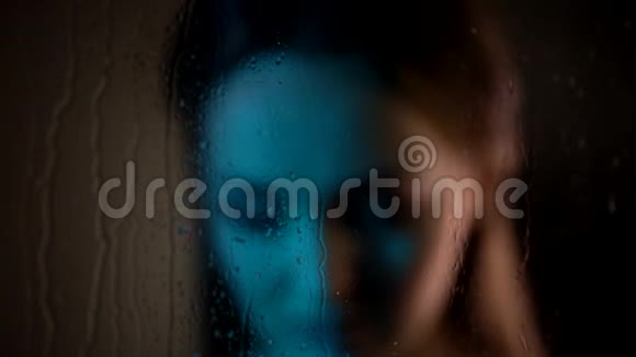 近距离拍摄梦幻悲伤迷人的白种人女人站在蒸汽窗户玻璃旁边看着雨滴飘落视频的预览图