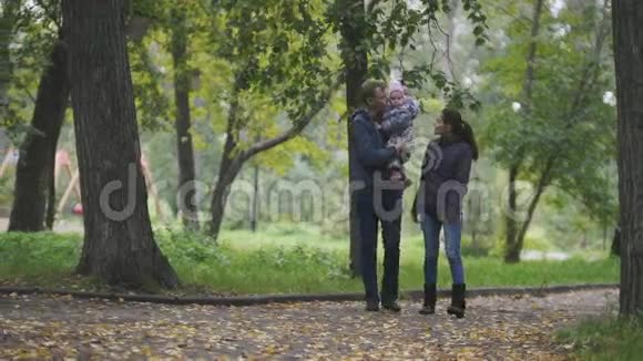 幸福的家庭秋天公园里的爸爸妈妈和小女孩带着落叶走过小巷视频的预览图