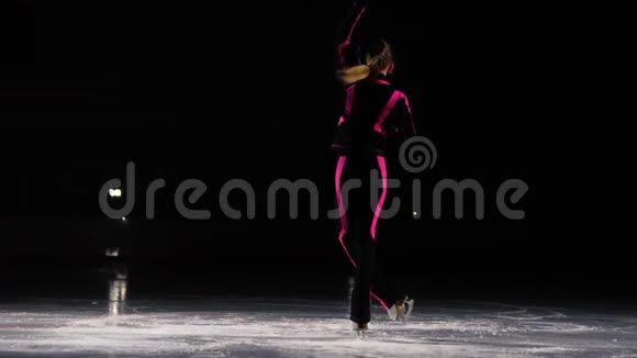 一个穿着黑色运动服和白色溜冰鞋的小女孩在冰场的竞技场上表演旋转台视频的预览图
