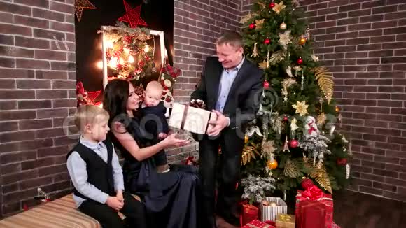 丈夫送礼物给妻子和孩子家庭中的圣诞聚会父亲母亲和婴儿在圣诞节附近视频的预览图