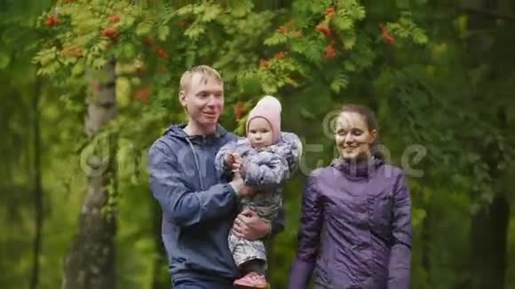 快乐的家庭爸爸妈妈和秋天公园里的小女孩爸爸妈妈和宝宝在罗文周围摆姿势关门视频的预览图