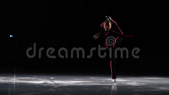 一个穿着黑色运动服和白色溜冰鞋的小女孩在冰场的竞技场上表演旋转台视频的预览图