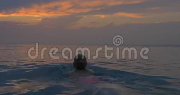 在日落时分年轻女子在大海中游去神奇地看到傍晚多云的天空和平静的大海视频的预览图