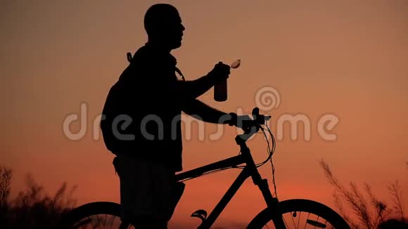 Cyclist从他的食堂喝水日落时的剪影视频的预览图