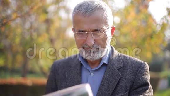 老人在公园里看报纸秋天黄树的背景视频的预览图