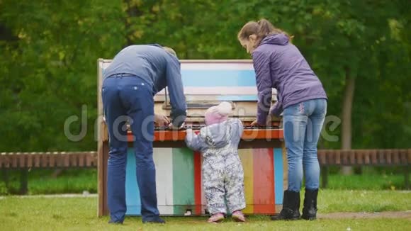 幸福的家庭爸爸妈妈和小女孩走在秋天的公园里在钢琴附近演奏视频的预览图