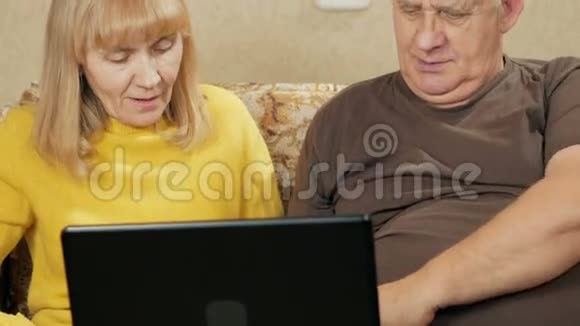 成熟的一对夫妇把笔记本电脑放在家里的沙发上丈夫和妻子正在电脑屏幕上浏览新闻视频的预览图