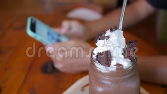 年轻女子在前面的甜巧克力甜点咖啡屋的智能手机上看照片高清视频的预览图