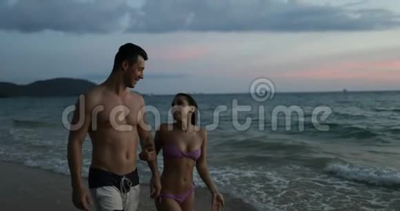 一对情侣在沙滩上散步在日落后牵手幸福的男人和女人在海边度假视频的预览图