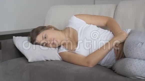 3一位患胃痛的年轻妇女躺在客厅的沙发上视频的预览图