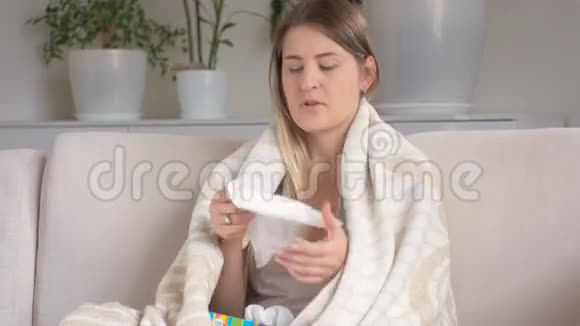 患流感的年轻患病妇女用毯子盖着用纸纸巾吹鼻子视频的预览图