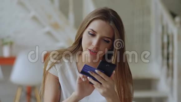 美丽的年轻女性在家使用智能手机和信用卡进行网上银行和购物视频的预览图