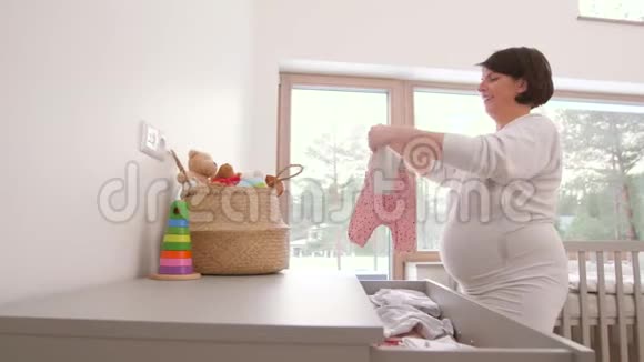 快乐的孕妇在家里套婴儿衣服视频的预览图