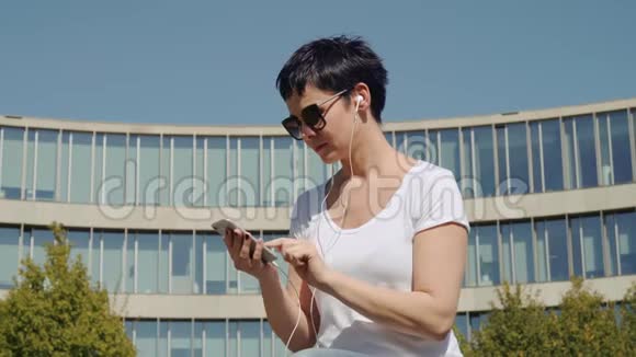 商务女性坐在办公楼前听电话里的音乐视频的预览图