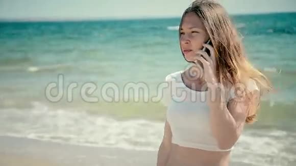 美丽的年轻女子穿着比基尼在海边玩智能手机阳光明媚的夏天在海边视频的预览图