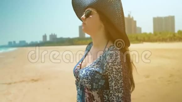海滩上穿着蓝色连衣裙的女孩看着海洋摘下蓝色帽子近距离射击视频的预览图