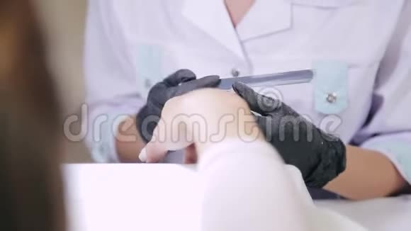 一名戴手套的美甲师在涂抹凝胶涂层之前用指甲锉钉客户视频的预览图